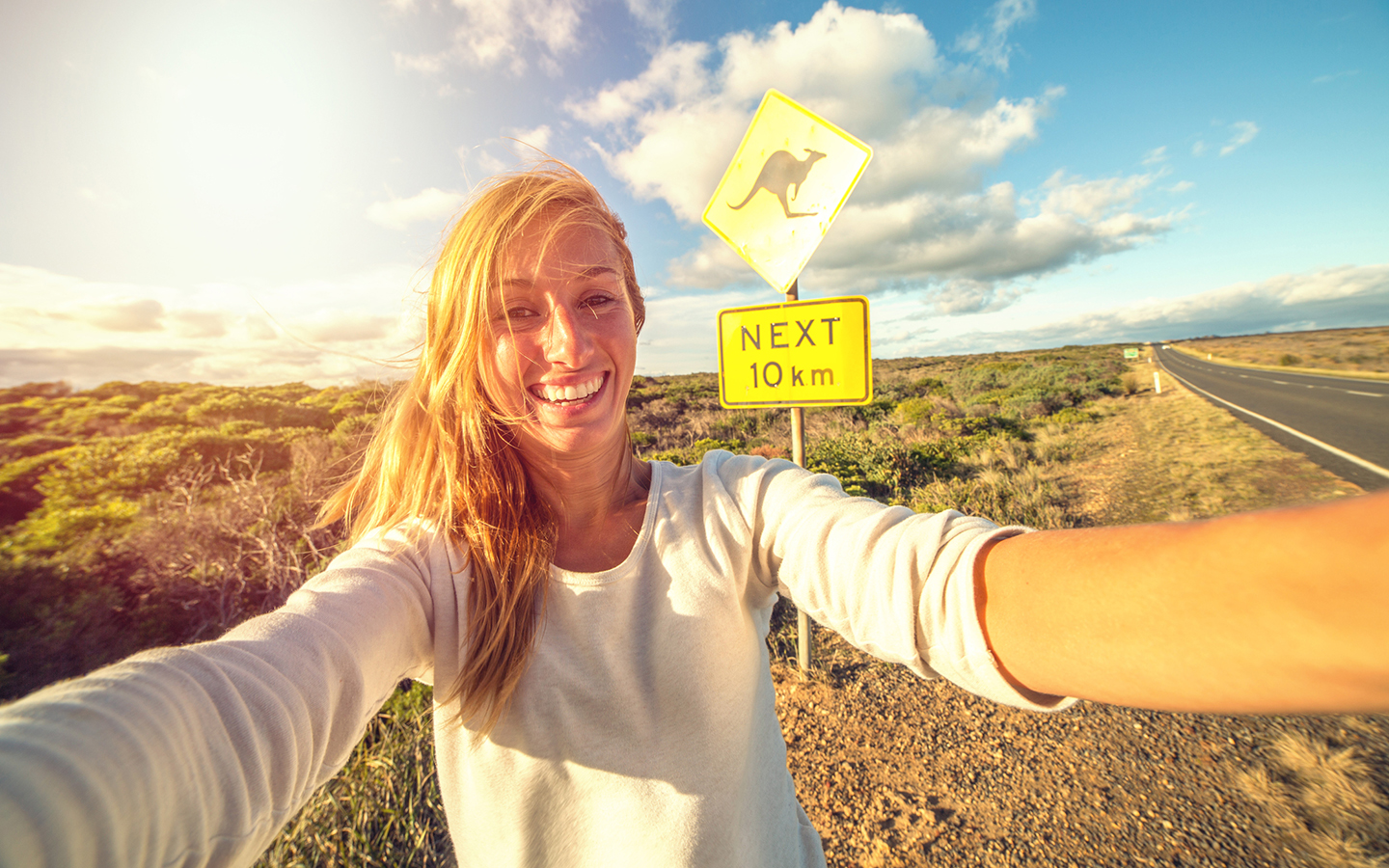 Woman on the side road in Australia next to a Kangaroo crossing sign while on a work abroad visa.