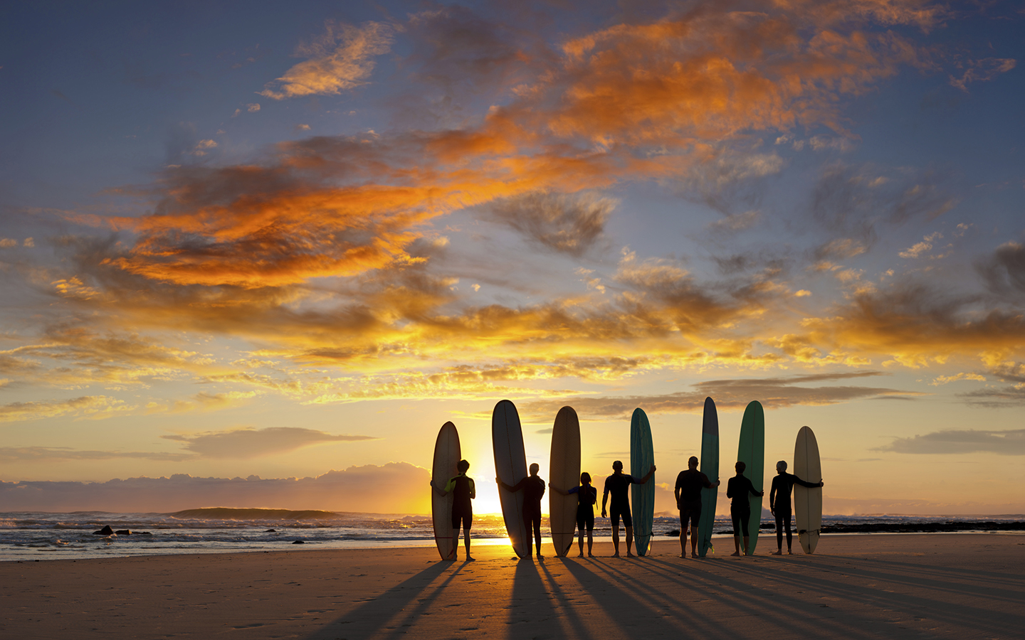 Group of friends stand on the Australia beach at sunset with their surf boards.