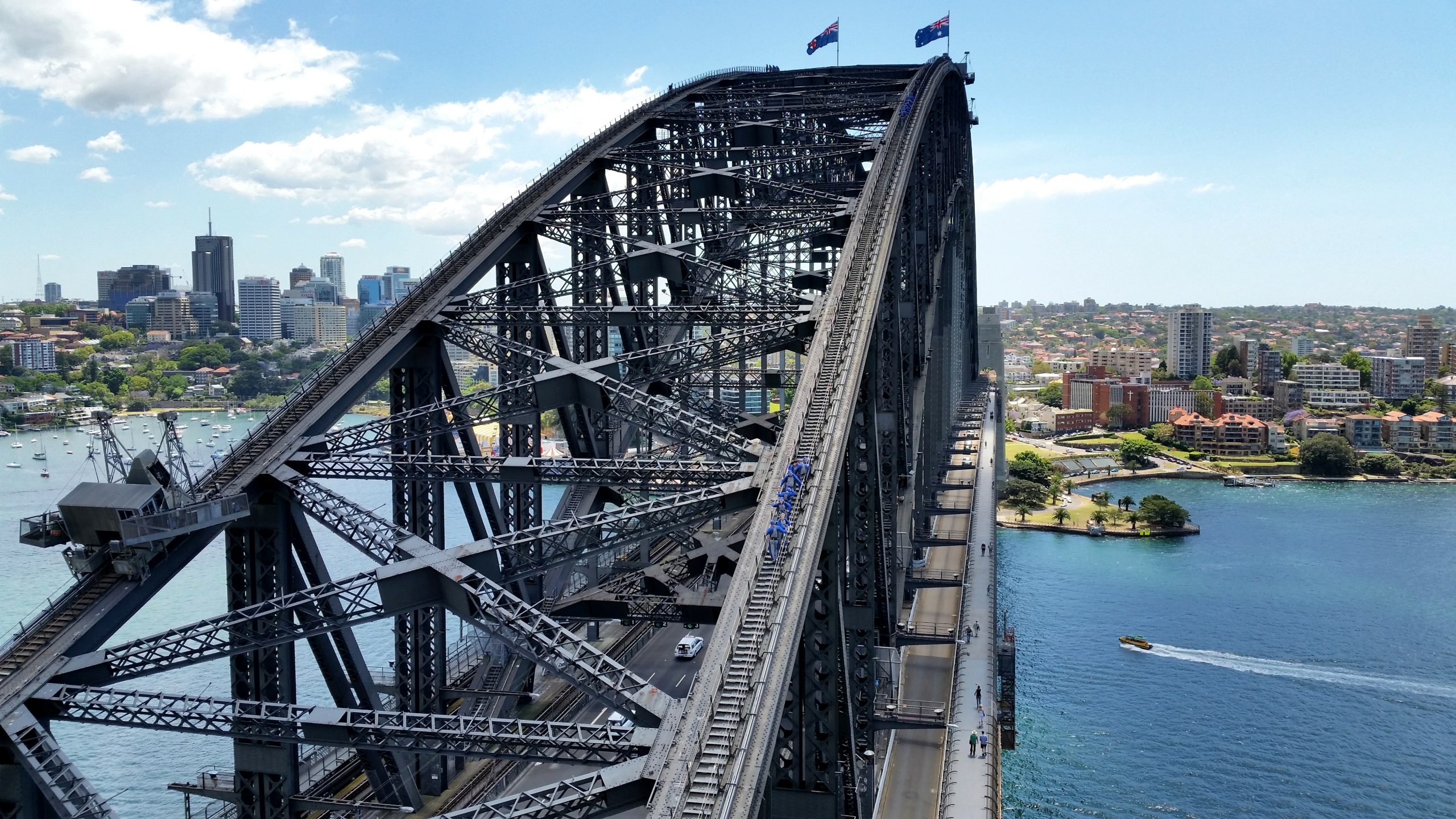 Climbers walk up the Sydney Harbour Bridge on a sunny day.