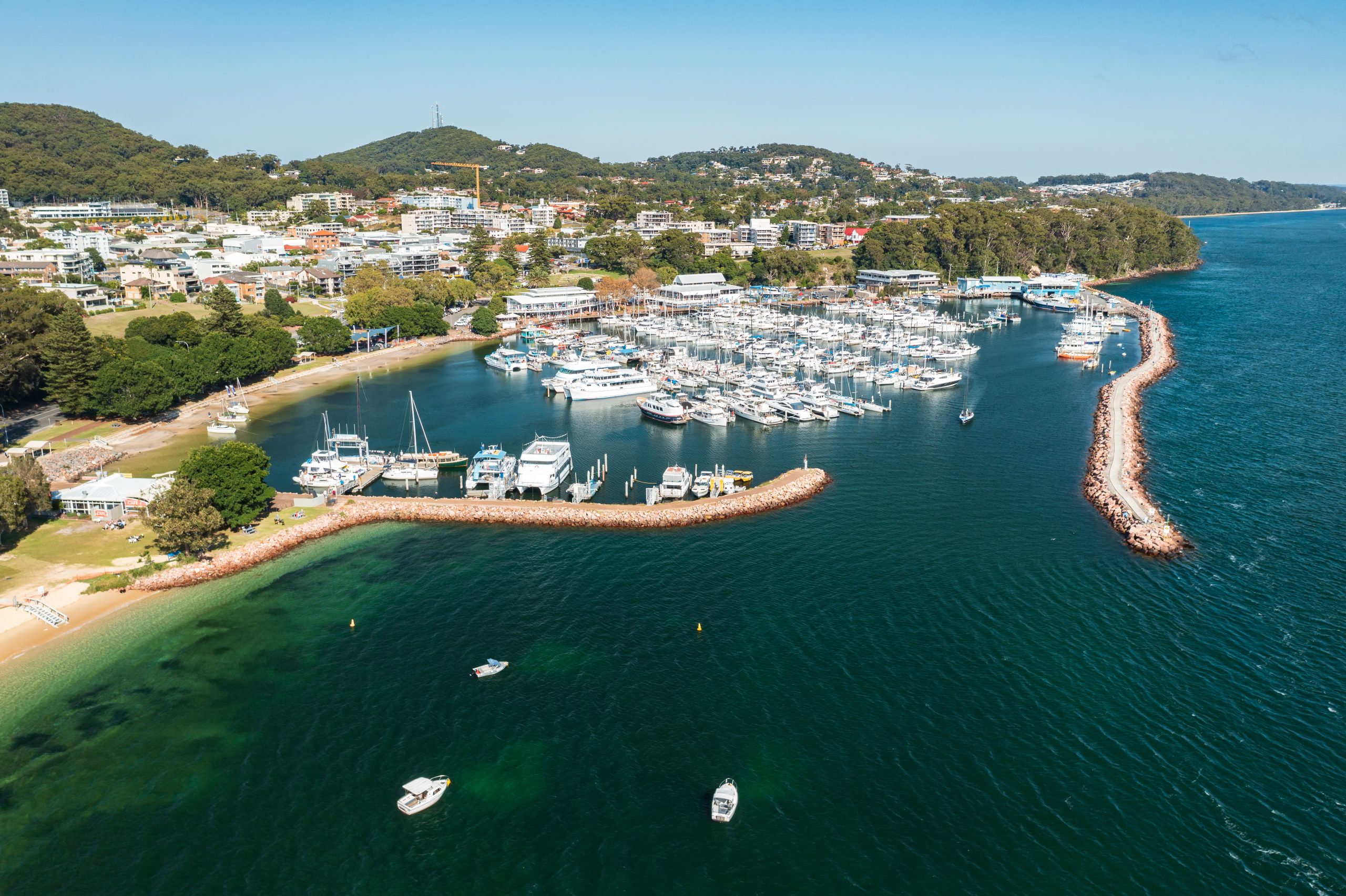 Aerial view of Nelson Bay marina, breakwater, and town, with aqua waters of Port Stephens, Australia.