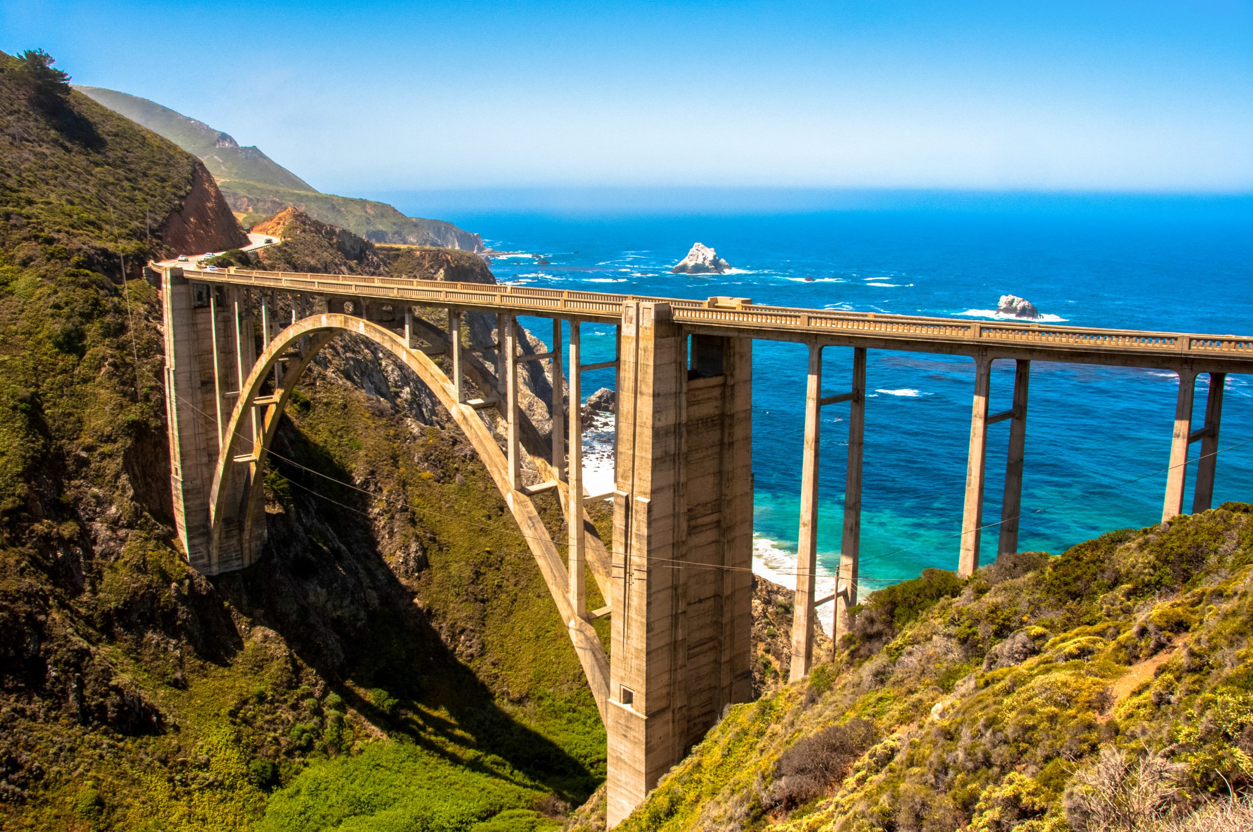 Big Sur on a sunny day with Bixby Bridge in the foreground and bright blue California waters behind it.