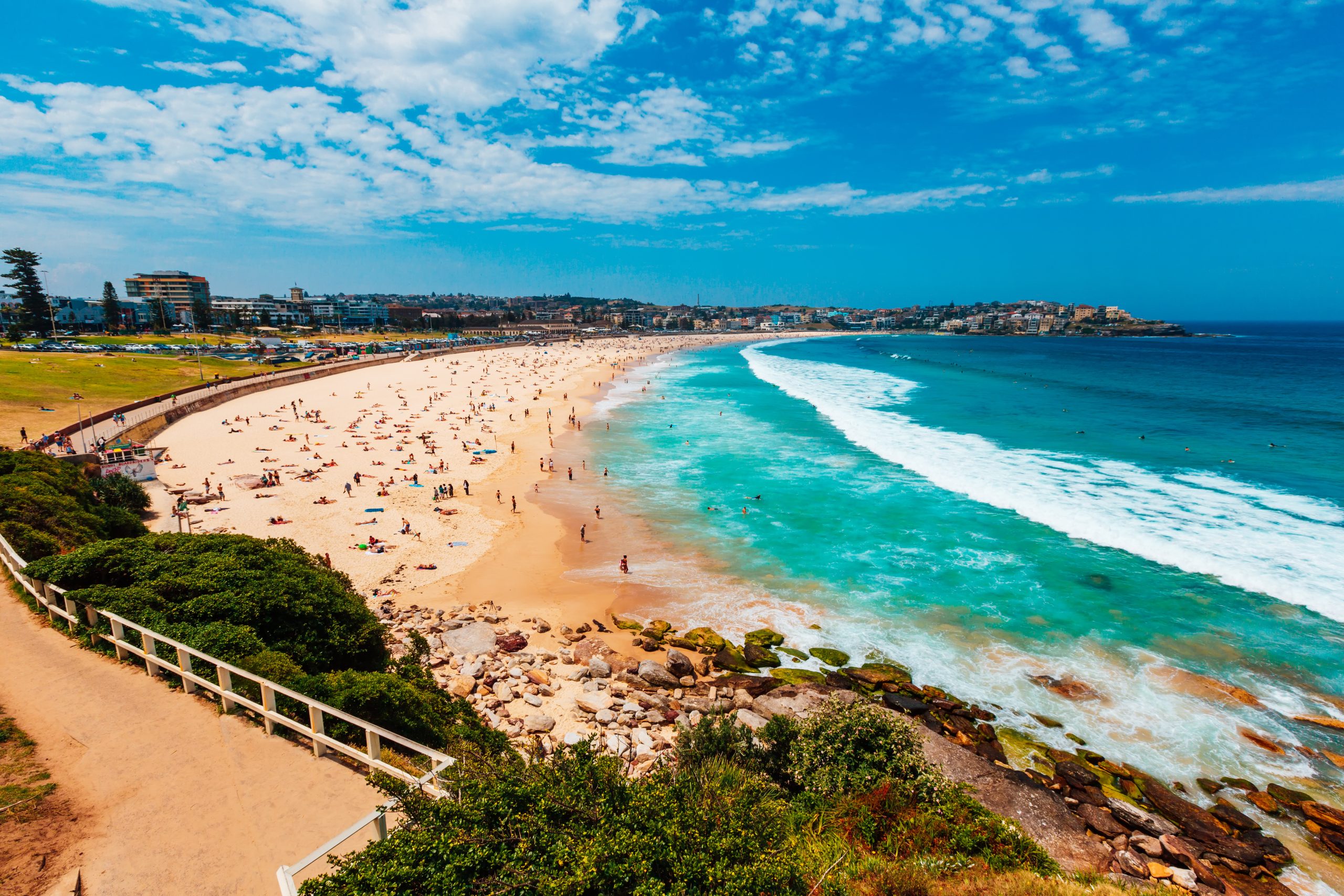 Sunny day at Bondi Beach in Sydney, NSW, Australia. The beach is full of people and the water is bright blue.