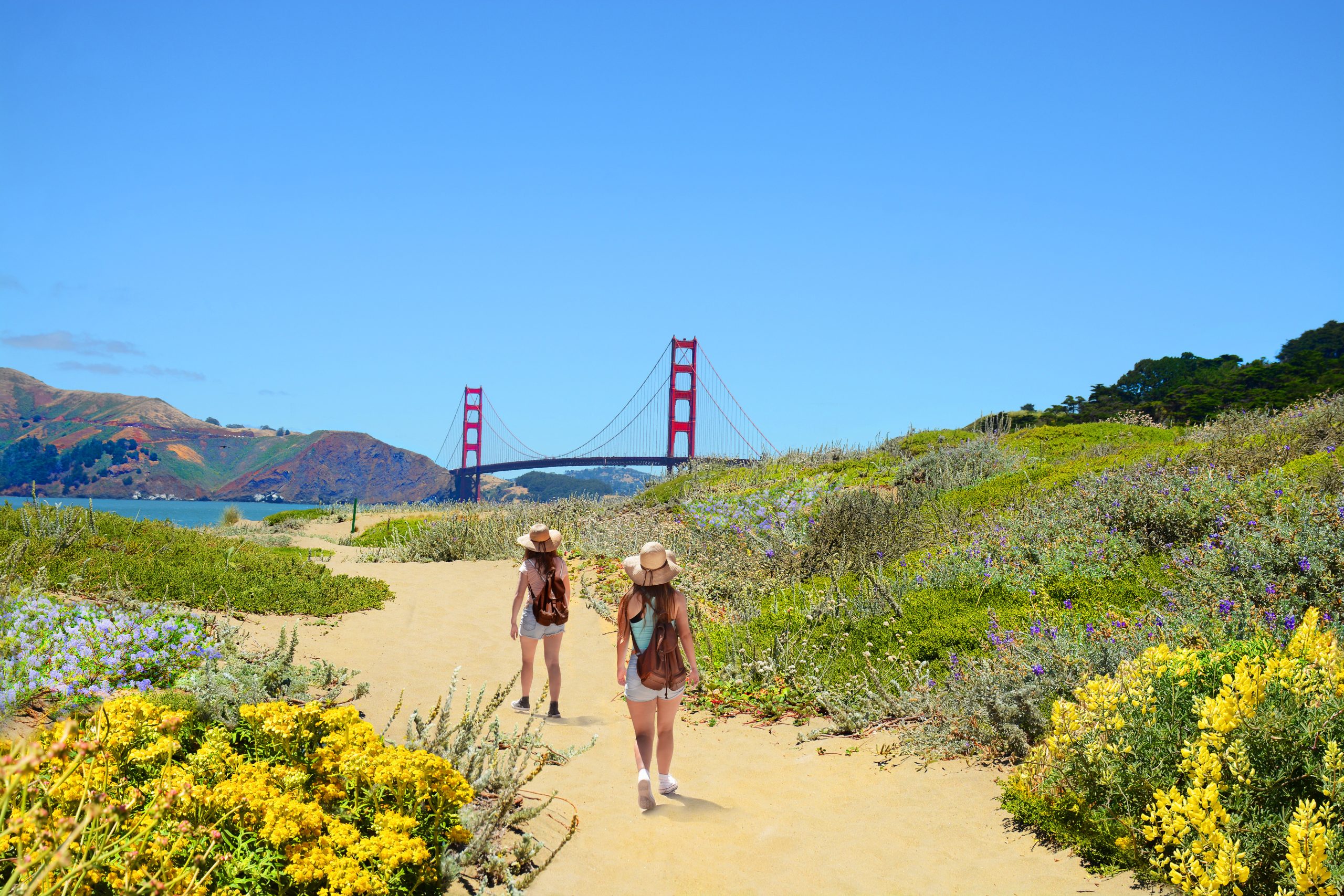 Two friends hike on a sandy trail towards the Golden Gate Bridge in San Francisco, California