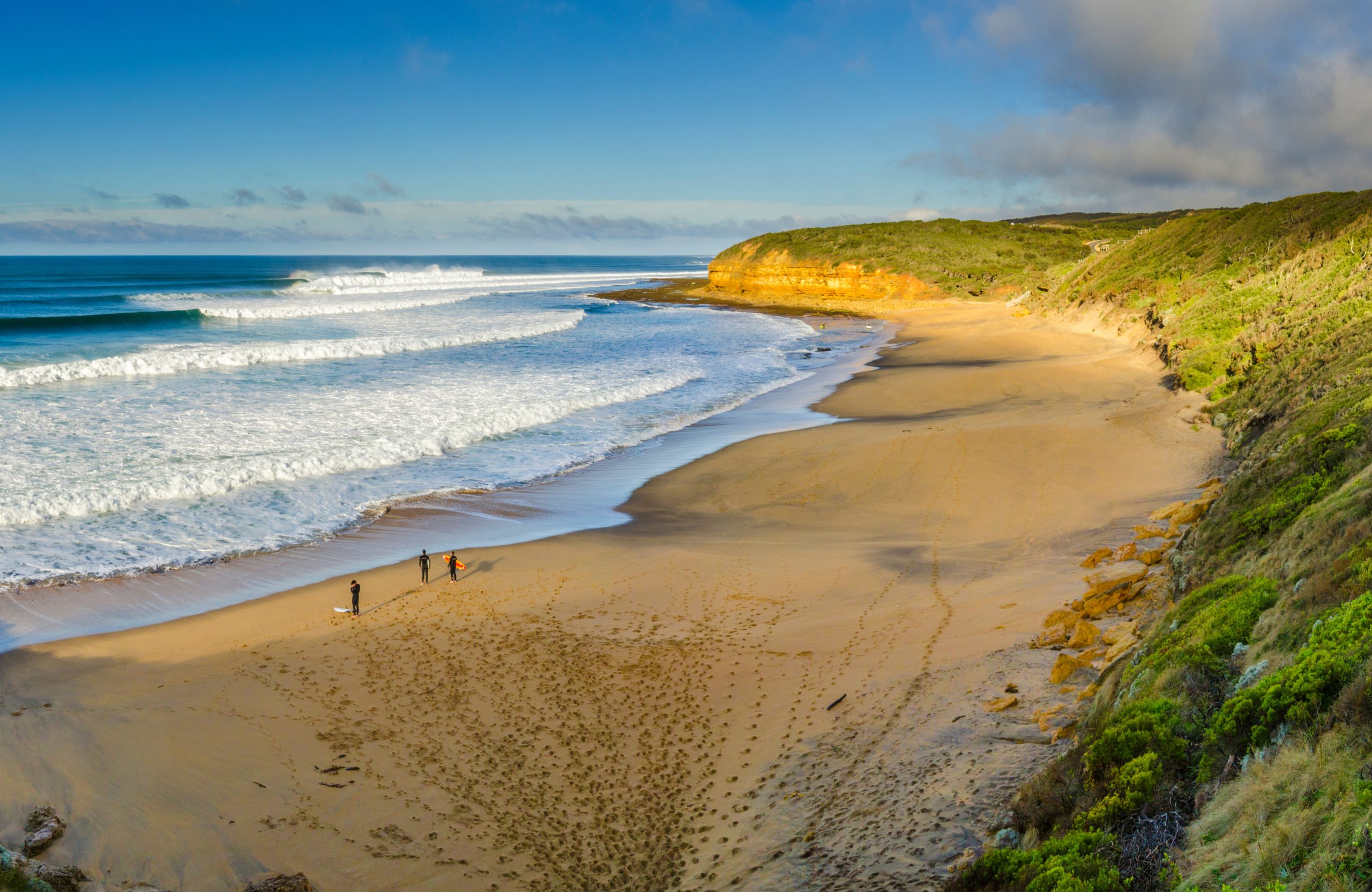 A sunny day at Bells Beach in Victoria, Australia with a small group of surfers standing on the waters edge about to go surfing.