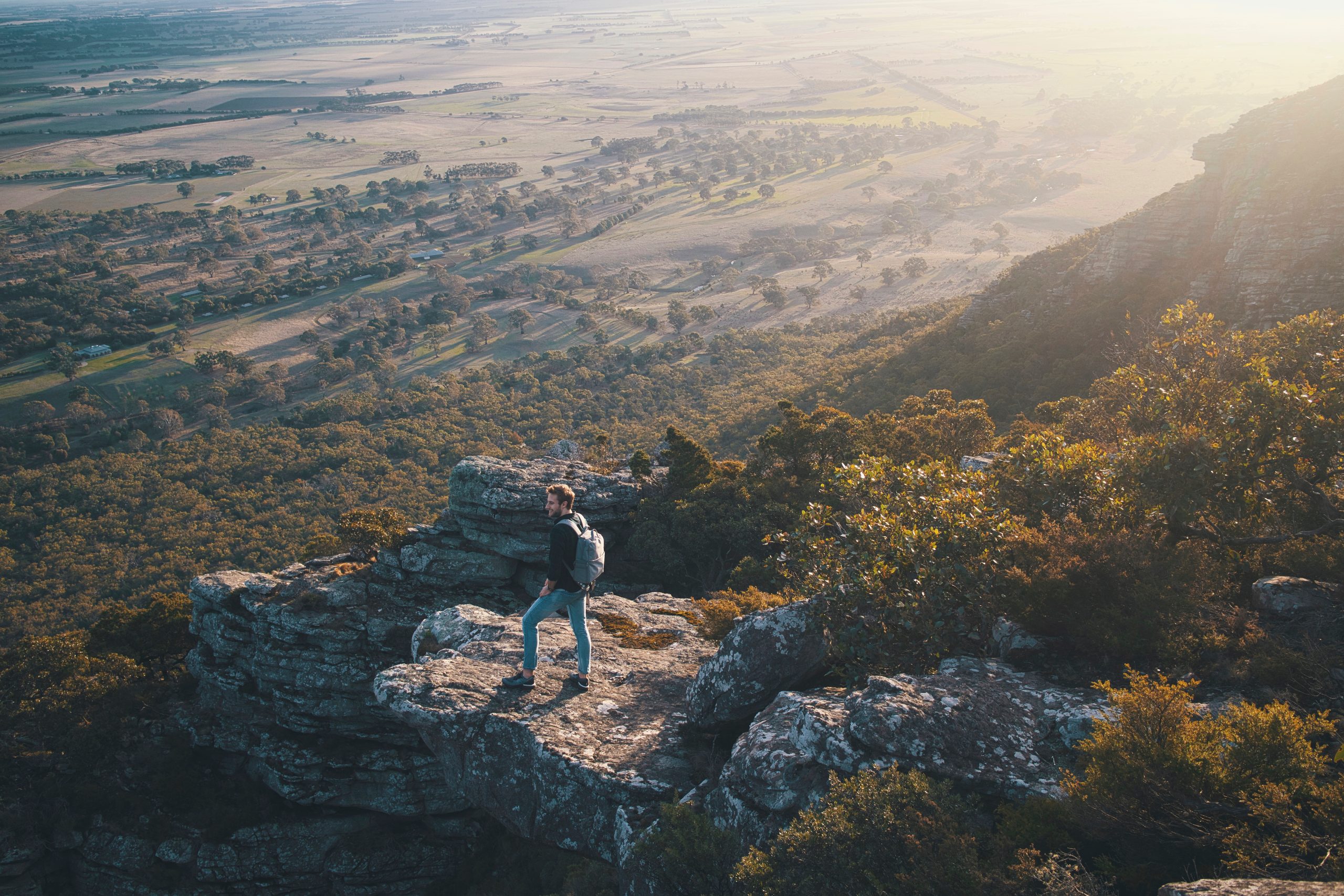 Young guy standing cliffside in Grampians National Park in Victoria, Australia overlooking a valley.