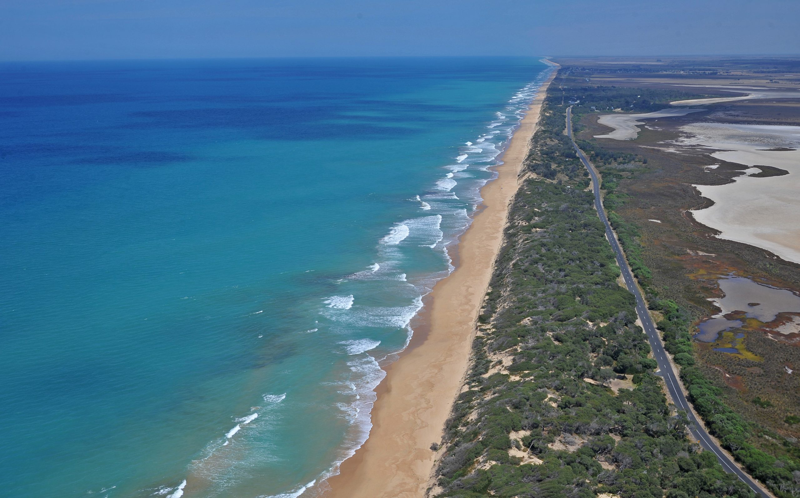 Aerial view of Ninety Mile Beach in Victoria Australia, with the light sand and light blue waters stretching out into the distance.